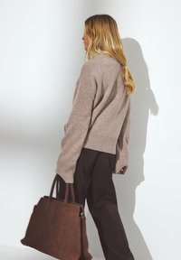 Light brown oversized sweater with ribbed hem, paired with dark wide-leg trousers. The person holds a dark brown leather tote bag.