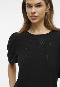 Svart kortärmad topp i texturerat tyg med ett intrikat mönster och puffärmar, rundad halsringning och avslappnad passform.