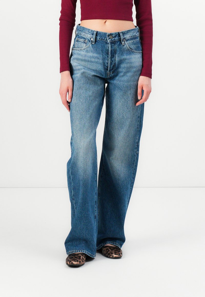 Modre široke jeans hlače iz denima, z bledejšim pranjem, klasičnim dizajnom s petimi žepi in visokim pasom, v kombinaciji z leopardjimi čevlji.