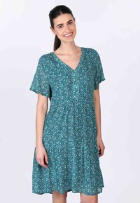 V-Ausschnitt, kurzärmeliges Kleid aus leichtem Stoff mit teal-farbener Basis und floralem Muster in Lila und Grün. Schwingendes Rockdesign.