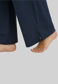 Navy blauwe broek met een ontspannen pasvorm en zijsplits aan de zoom; gecombineerd met blote voeten die netjes onderhouden nagels tonen.