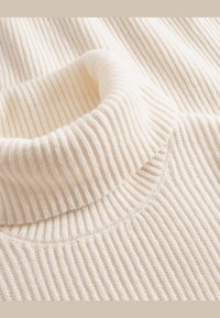 Pull à col roulé crème côtelé avec un tricot doux et texturé. Caractérisé par un col haut et un encolure lisse et arrondie.