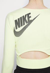 Fluoreszcens sárga Nike crop top, hosszú ujjakkal, nyitott hátú kialakítással és egy nagy fekete pöttyös swoosh logóval a háton.