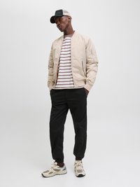 Beige bomberjakke,stripet skjorte, svarte tapered bukser og beige sneakers. Tilbehør inkluderer en svart og nettingcaps. Enkelt design, avslappet utseende.