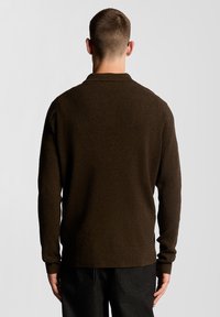 Σκούρο καφέ πλεκτό πουλόβερ με ριμπ υφή, μακριά μανίκια και κλασικό γιακά. Η πίσω όψη δείχνει άνετη εφαρμογή και καθαρές γραμμές.