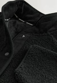 Black, textured jacket featuring a collar of ribbed fabric, a soft fleece body, and a snap closure detail. Interior label reads "downtime."