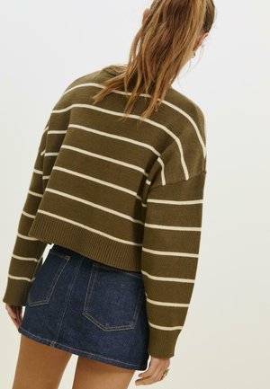 Maglione cropped a righe marroni e bianche con polsini a costine, abbinato a una mini gonna di denim scuro con tasche posteriori e cuciture in vista.