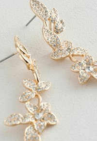 Zlatne floralne naušnice s prozirnim rhinestones, s poliranom završnom obradom i detaljnim oblicima listova. Uključena metalna potpora.