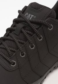 Scarpa sportiva nera realizzata in materiale sintetico testurizzato, con lacci spessi, occhielli esagonali e un colletto imbottito per il supporto.