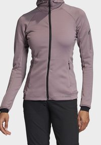 Chaqueta deportiva morada con cremallera completa, tela texturizada, diseño ajustado, cuello alto y bolsillos laterales con cremallera. Logo de la marca en el dobladillo.
