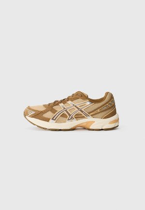 Chaussure de sport marron et beige avec des accents de logo blancs et argent réfléchissants, design à lacets et semelle rembourrée sur un fond gris clair uni.