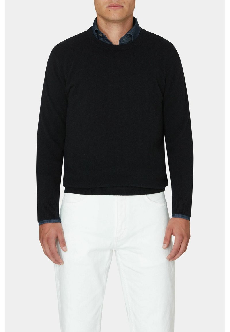 Schwarzer gestrickter Pullover mit rundem Halsausschnitt, langen Ärmeln und gerippten Bündchen, kombiniert mit weißen Hosen und einem blauen Button-Down-Hemd darunter.