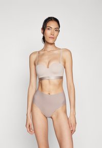 Lys beige lingeri-sæt med en formet bralette med tynde stropper og et logo-bånd, parret med højtaljede sømløse trusser i en matchende nuance.
