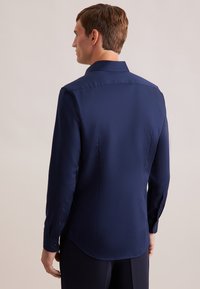 Camicia a maniche lunghe blu navy in tessuto morbido e strutturato, con colletto a punta e polsini abbottonati. Presenta un orlo curvo e una silhouette aderente.