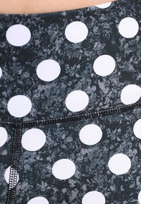 Tejido negro con una textura moteada que presenta grandes lunares blancos. Detalles de costura a lo largo del borde.