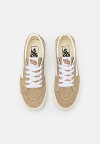 Sneaker in suede marrone con lacci bianchi, suola in gomma beige e etichetta logo Vans. Presenta dettagli perforati e cuciture a contrasto.
