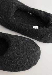 Black slippers made of soft, fuzzy felt featuring a round toe and minimal stitching. Include subtle metallic fiber accents.