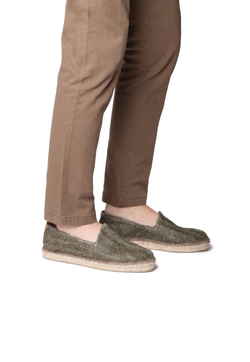 Espadrilky v tmavozelenej tkanine s okrúhlou špičkou, jute medzipodrážkou a elastickými stranami, v kombinácii s khaki bavlnenými nohavicami.