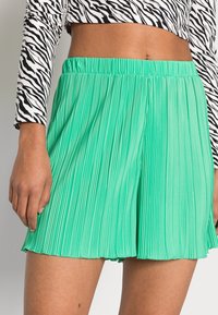 Plisserede mintgrønne shorts med elastisk talje, der har en glat tekstur og en udvidet silhuet. Sort-hvid zebra print crop top synlig.