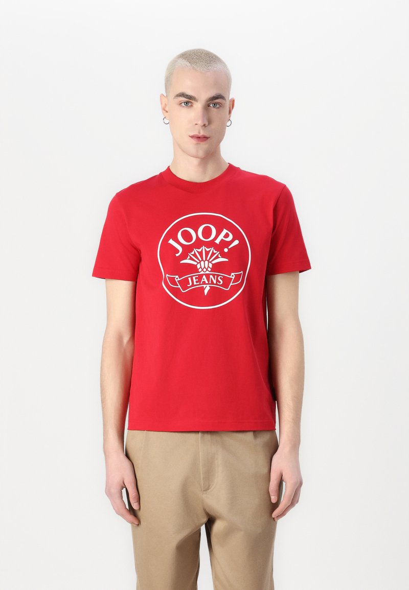 T-shirt en coton rouge avec un logo rond blanc et le texte "JOOP! JEANS". Manches courtes et design classique à col rond.