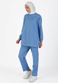 Light blue tracksuit made of soft fabric, featuring a loose-fit top with long sleeves and matching pants. Includes white sneakers.