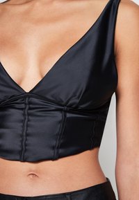 Černý saténový crop top s hlubokým výstřihem do V, strukturovanými švy a pouzdrovým střihem, spárovaný s černými kalhotami s vysokým pasem.