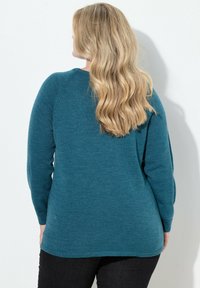 Turbogras langer Strickpullover mit Rundhalsausschnitt, Raglanärmeln und leicht abgerundetem Saum. Die glatte Textur sorgt für subtile Wärme.