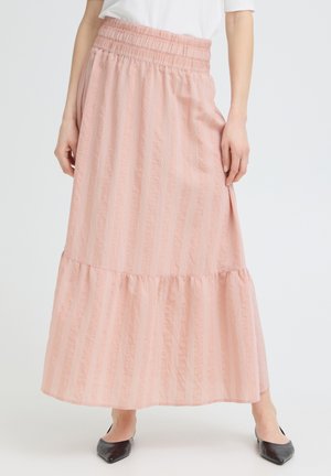 Femme portant une jupe longue couleur pêche à rayures verticales avec un ourlet à volants et une taille froncée, associée à des ballerines noires à bout pointu.