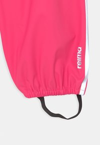 Różowe wodoodporne spodnie z elastycznymi mankietami i czarnym zapięciem. Posiadają srebrne boki i logo "reima" w białym kolorze. Gładka tekstura.