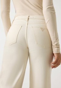 Τζιν παντελόνι εκρού με ψηλή μέση, ομαλή υφή, δύο πίσω τσέπες και τρίγωνο λογότυπο στην δεξιά τσέπη.