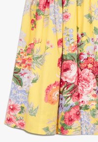 Květinová tkanina má jasné růže v červené, růžové a oranžové barvě na žlutém pozadí, se zelenými listy a světle modrými akcenty.