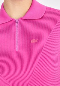 Rosa zip-up tröja med ribbat mönster och krage. Har en liten, tonad logotyp på vänster sida.