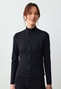 Giacca nera con zip realizzata in un materiale liscio e stretch. Presenta un collo alto, maniche lunghe e tasche laterali. Design aderente.