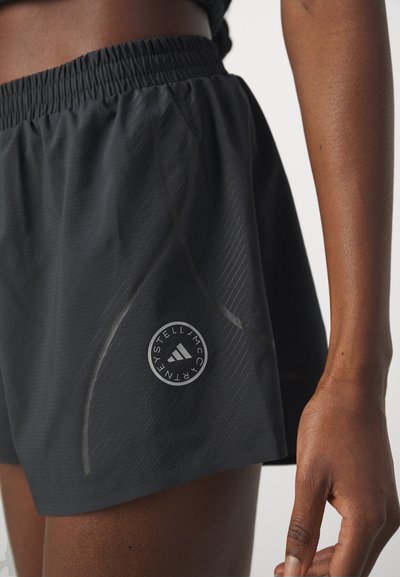 Schwarze Sportshorts mit elastischem Bund und rundem Logo am Oberschenkel, getragen von einer Person mit dunkler Haut und sichtbarem Arm.