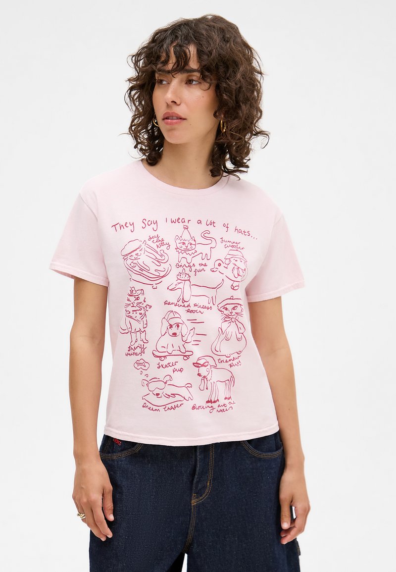 Light pink T-shirt featuring playful, red line-drawn illustrations of animals wearing various hats and a humorous text caption.