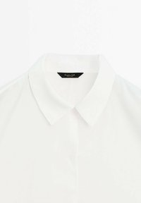 Chemise blanche à col classique avec une texture lisse, dotée d'un col pointu et d'une fermeture à bouton, étiquetée "Massimo Dutti."