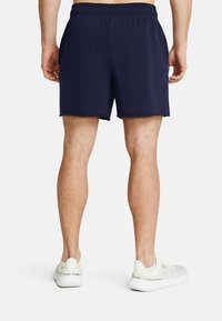 Marineblå idrottsshorts med elastisk midja, sidofickor och en slät textur, tillsammans med vita träningsskor.