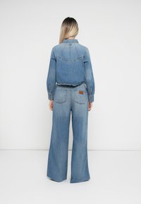 Denim outfit featuring a fitted blue denim shirt with long sleeves and high-waisted wide-leg jeans. Back view shows stitched details and patch.