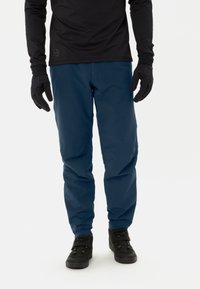 Waterdichte blauwe broek met een gladde textuur, in slim fit, met zakken, gecombineerd met zwarte handschoenen en schoenen met veilige riemen.