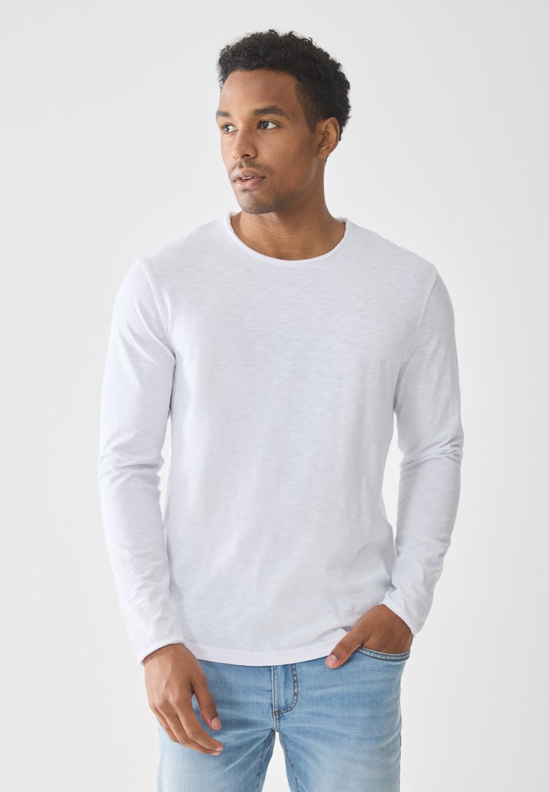 Biała, długosleeve koszulka z lekkiego, teksturowanego materiału z okrągłym dekoltem, zestawiona z jasnoniebieskimi dżinsami o luźnym kroju.