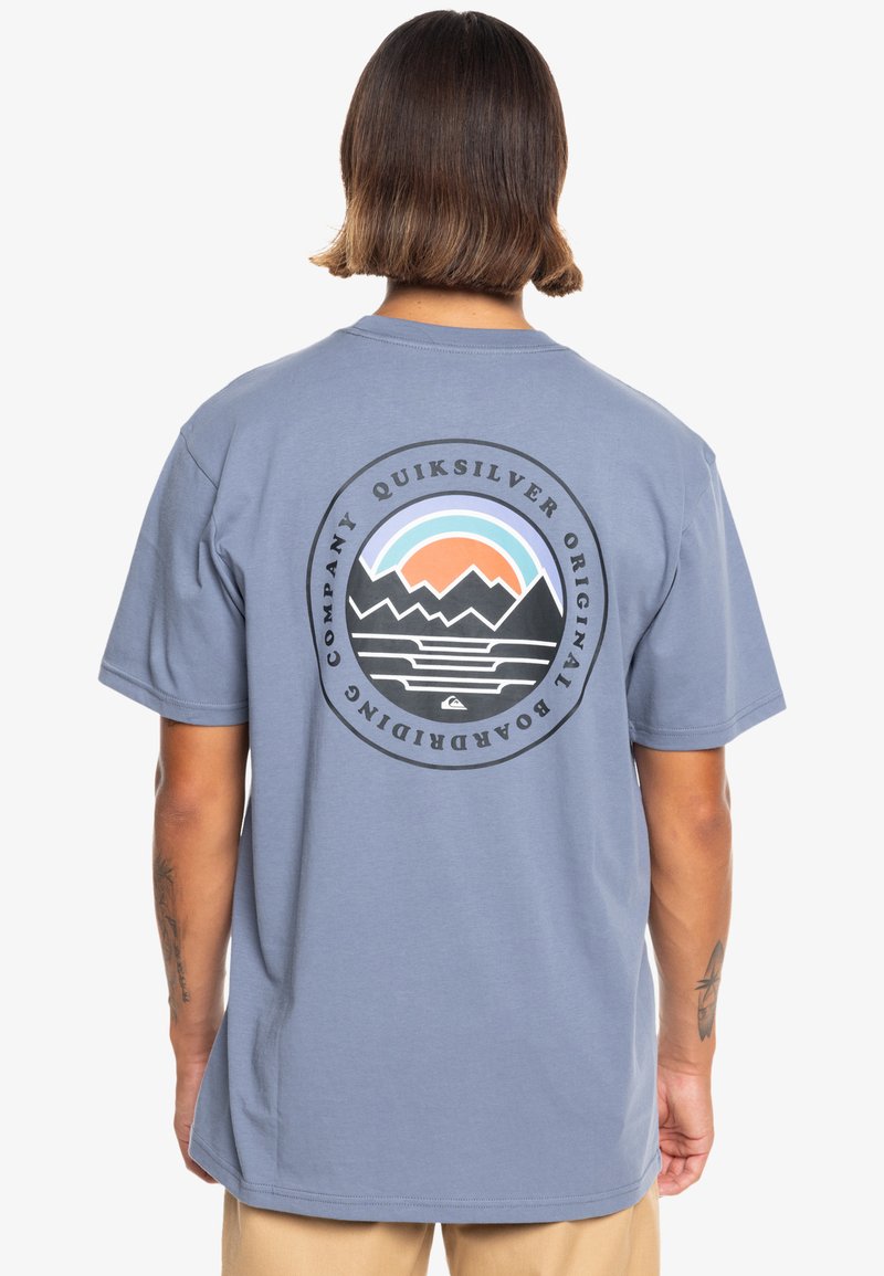 Light blue T-shirt with short sleeves featuring a circular mountain and sun graphic in black and pastel colors on the back.