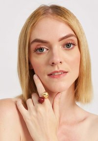 Złote i czerwone pierścionki na nagiej dłoni. Złoty pier�ścionek ma odbijającą powierzchnię, podczas gdy czerwony pierścionek jest gładki i błyszczący.