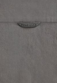 Grijze stof met een gestructureerde afwerking, met een opvallend "POLO CLUB" logo label genaaid in het midden bovenin. Eenvoudig en ingetogen ontwerp.