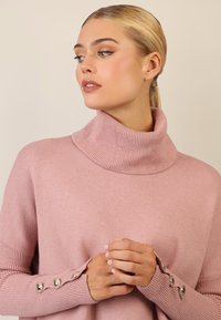 Hellrosa Rollkragenpullover mit Rippstruktur, ausgestattet mit drei dekorativen Knöpfen an jedem Ärmel und einer lässigen Passform.