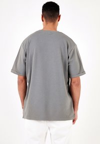 T-shirt grigio a maniche corte con vestibilità rilassata, texture a coste e maniche arrotolate. Il design presenta un collo rotondo e orlo piatto.