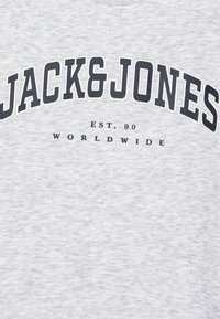 T-shirt gris à col rond, arborant "JACK&JONES" en grandes lettres foncées et "EST. 90 WORLDWIDE" en texte plus petit en dessous.