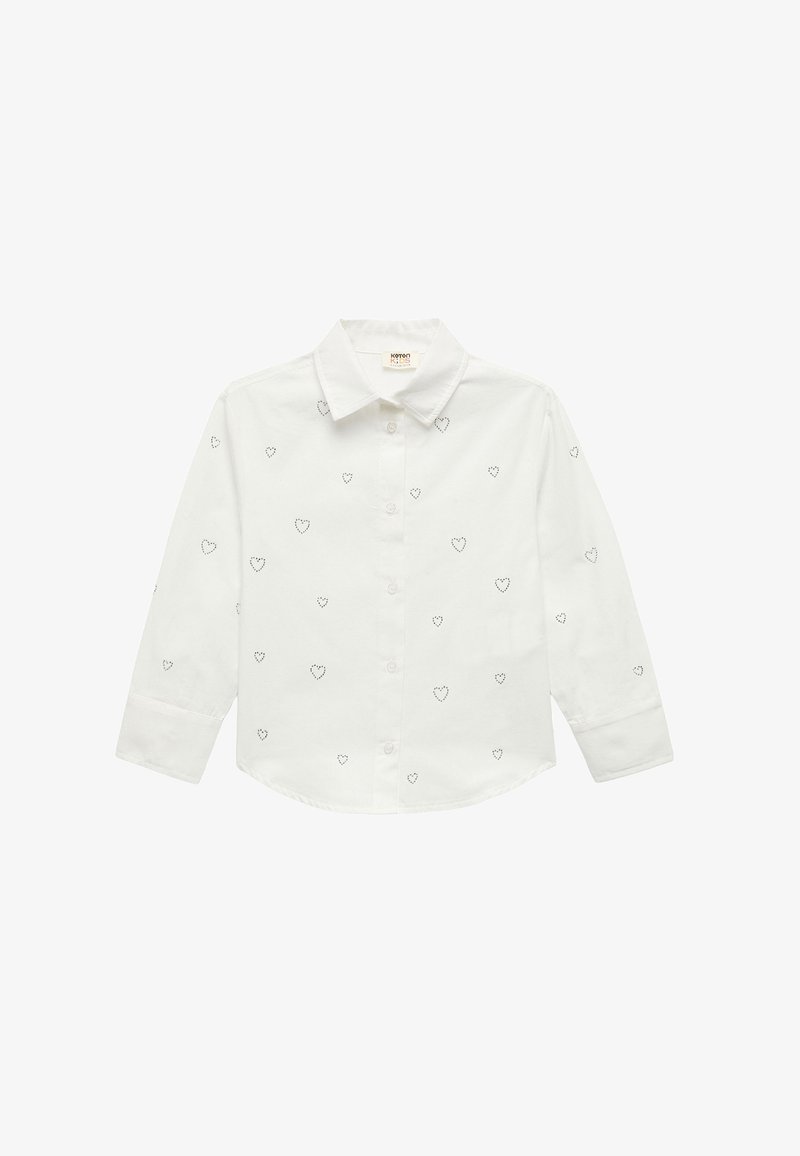 Chemise en coton blanche à boutons avec un col structuré et des manches longues, ornée de petits motifs en forme de cœur noir, régulièrement espacés sur le tissu.