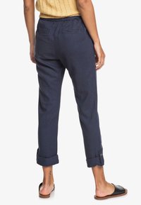 Pantalon en lin bleu marine avec une taille élastique, des ourlets retroussés et deux poches arrière. Texture lisse, design décontracté.