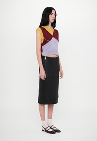 Krāsotu croppēto adījumu tops maroon, dzeltenā un purpursarkanā krāsā; melna ādas midi svārki; apvienots ar baltajiem zeķēm un tumšajiem apaviem.