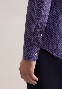 Camicia blu navy con un piccolo motivo circolare ripetuto in rosso e bianco; presenta polsini con bottone e una finitura liscia e strutturata.